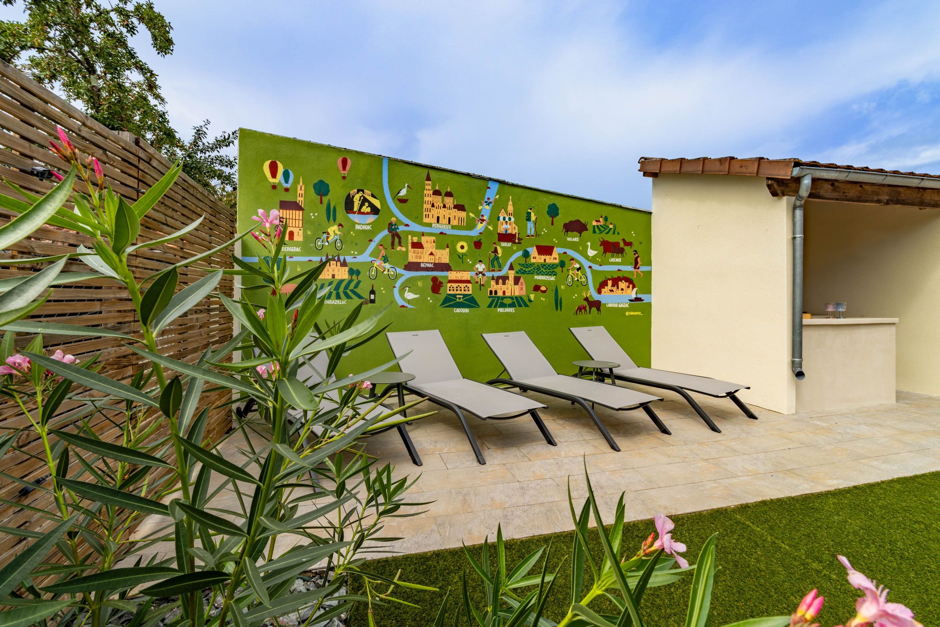 Un jardín con un mural, asientos al aire libre y una pérgola.