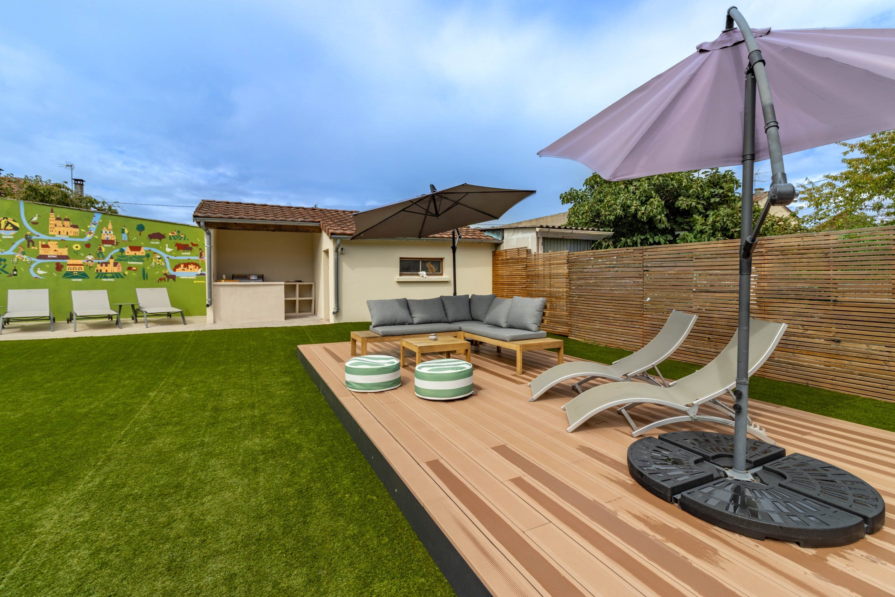 Un jardin avec une terrasse, du mobilier d’extérieur et une fresque murale.