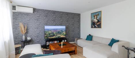 A modern living room with a flat-screen TV, a sofa set, a coffee table, and a bookshelf.