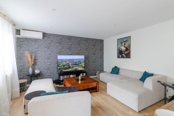 Una sala de estar moderna con un televisor de pantalla plana, un conjunto de sofás, una mesa de centro y una estantería.