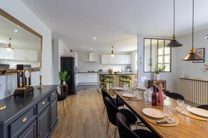 Una cocina moderna con armarios blancos, una zona de comedor con una mesa de madera dispuesta para cuatro personas y un espejo grande a la izquierda.