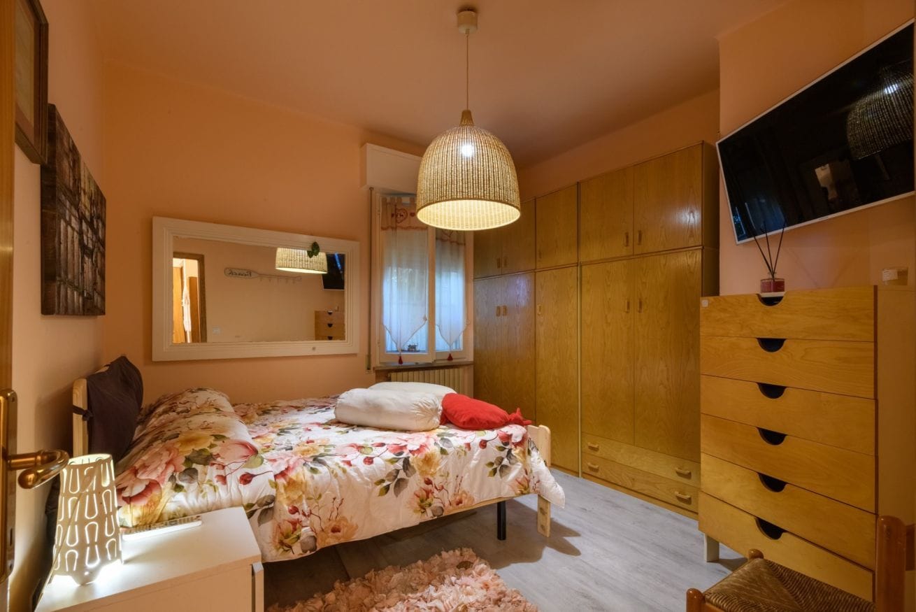 A bedroom with a bed, a wardrobe, a mirror, and a hanging light fixture.