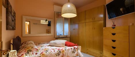 A bedroom with a bed, a wardrobe, a mirror, and a hanging light fixture.