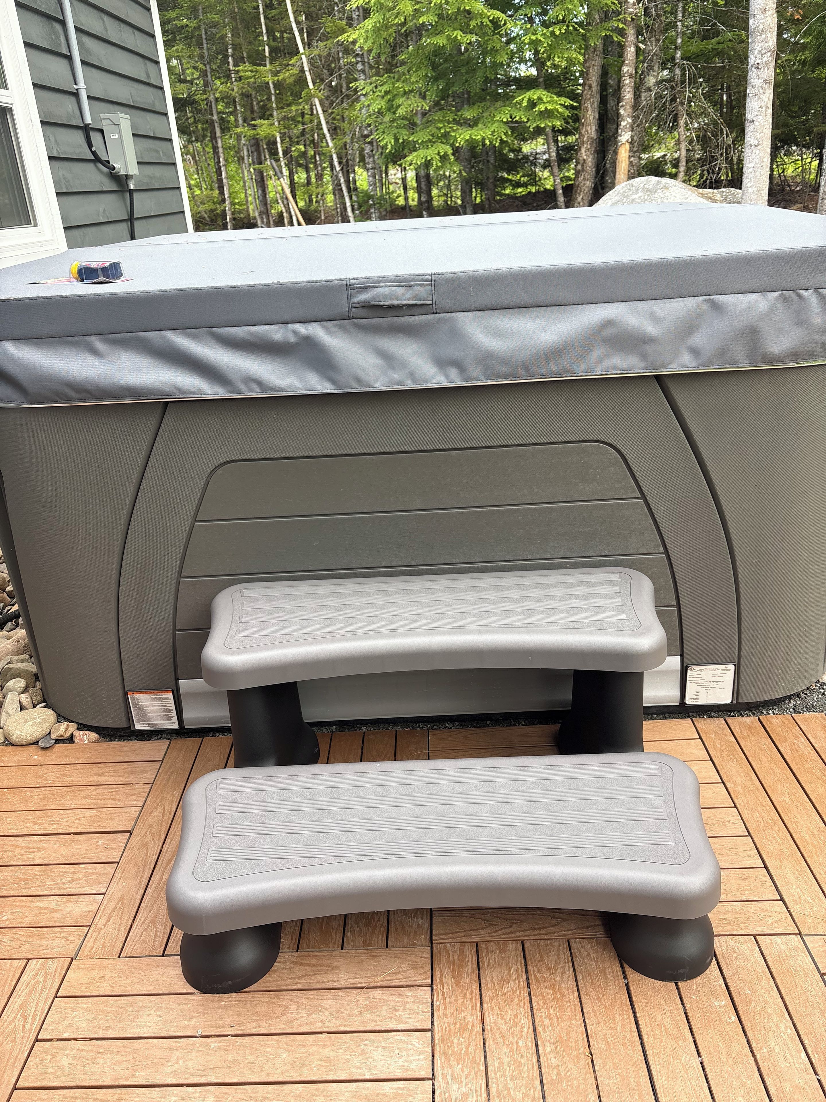 A hot tub with a cover, two steps leading up to it, and a wooden deck.