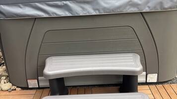 A hot tub with a cover, two steps leading up to it, and a wooden deck.