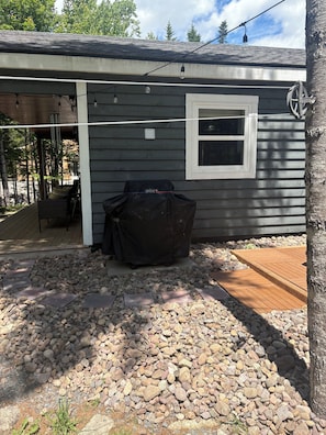 A covered outdoor area with a grill, a window, and a wooden deck.