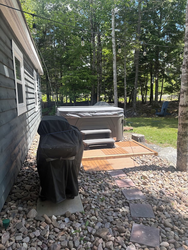 A backyard with a hot tub, a barbecue grill, and a deck.