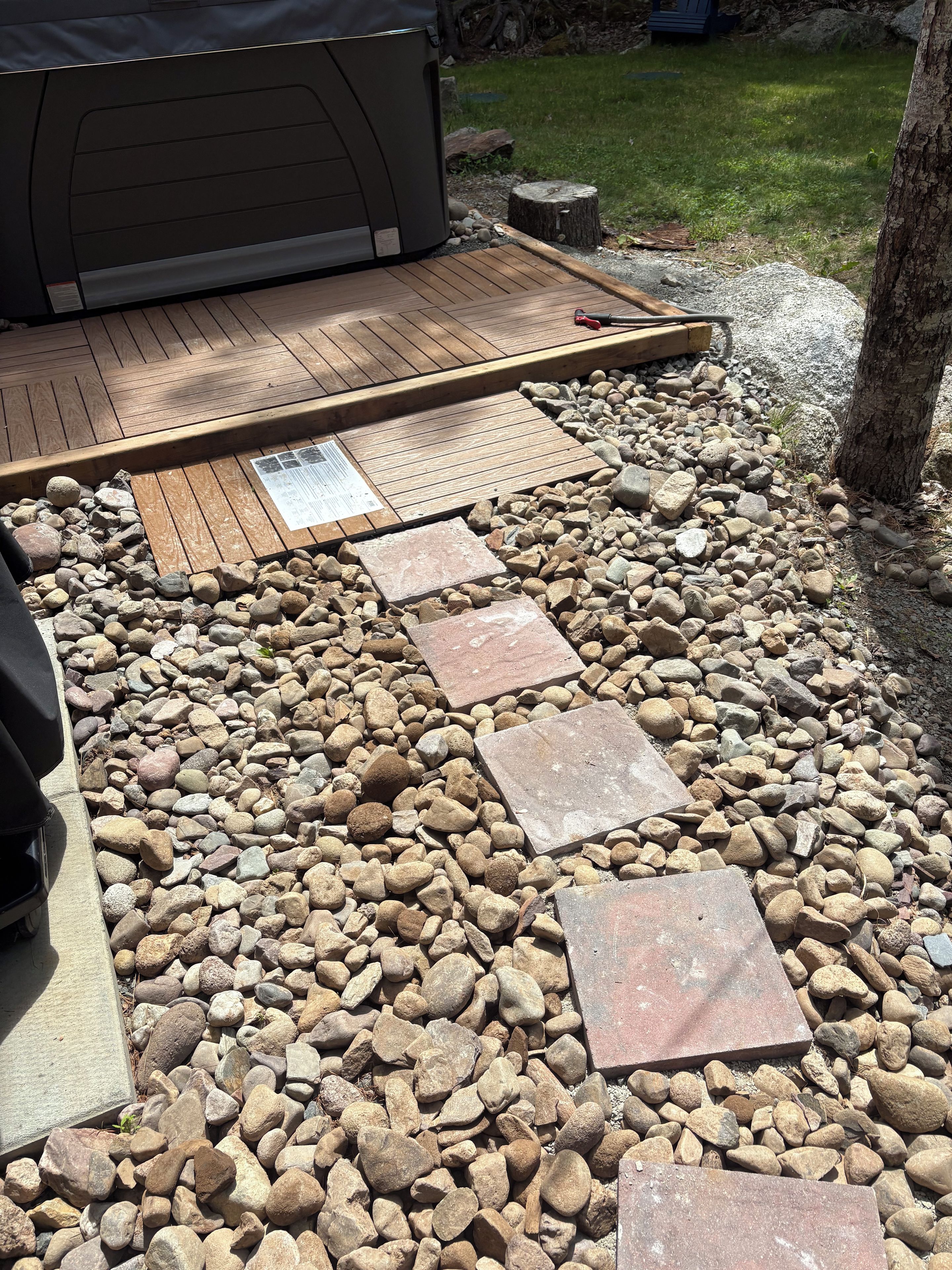 A patio area with a wooden deck, stone pathway, and a grill.
