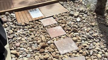 A patio area with a wooden deck, stone pathway, and a grill.