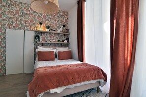 A bedroom with a bed, a wardrobe, shelves with decorative items, and a patterned wallpaper. - La Perle de Bon Secours - à 200 m de la plage (Saint-Malo)