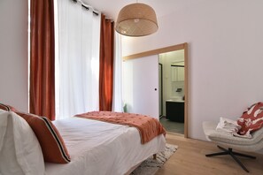 Une chambre à coucher avec un lit, une chaise, un luminaire suspendu et une vue sur une autre pièce.