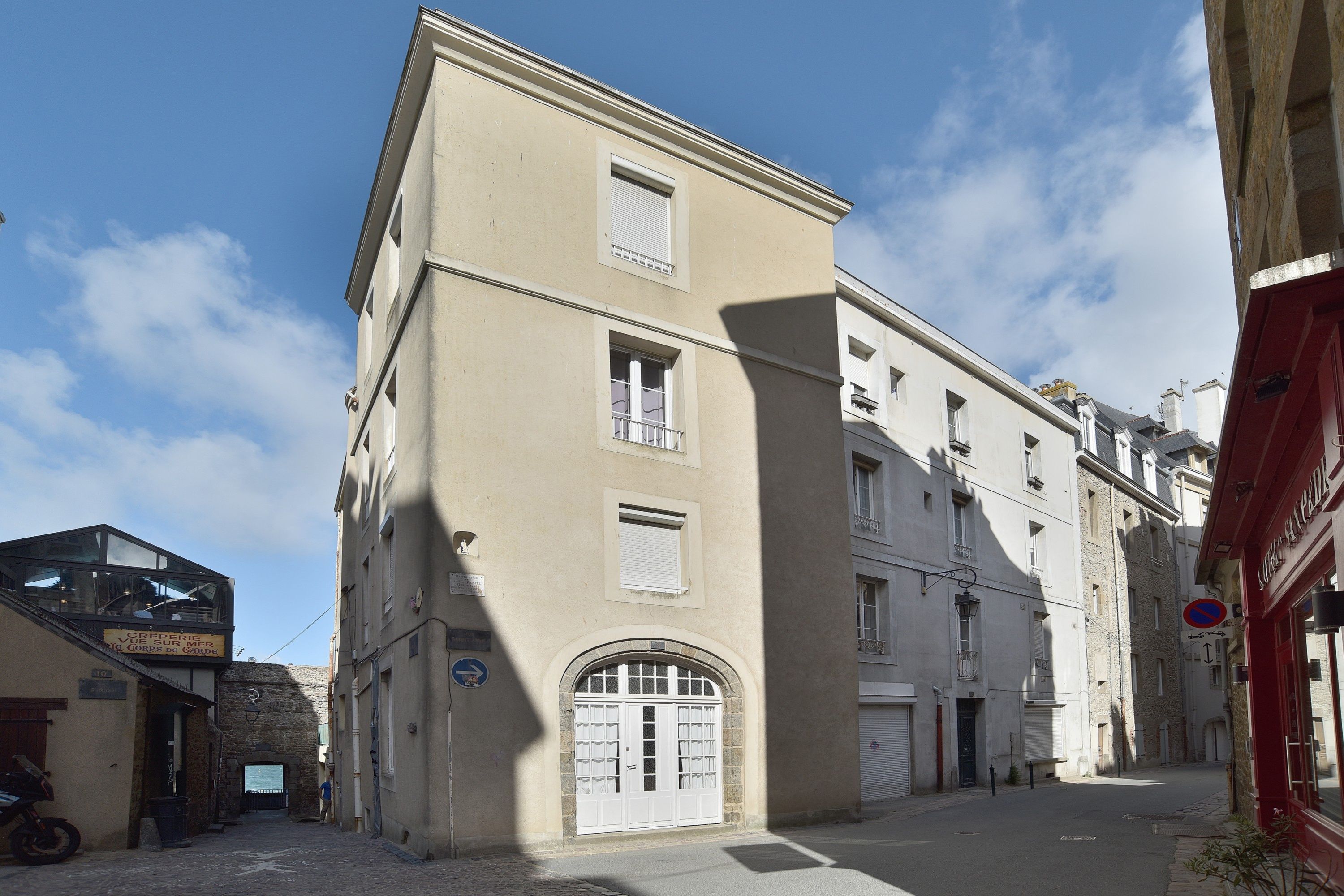 Un carrer estret amb un edifici que destaca per una entrada gran d'arc i nombroses finestres.
