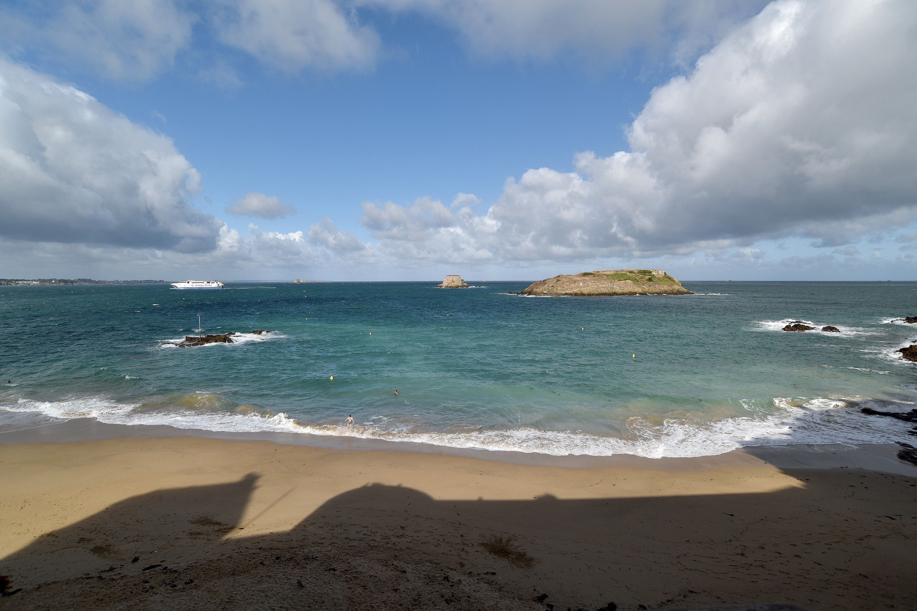 Una platja amb cel serè, mar tranquil·la i roques a la vora.