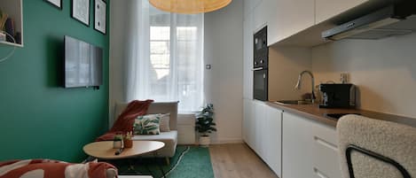 A compact living space with a kitchenette, a sofa, a small table, and a green rug.