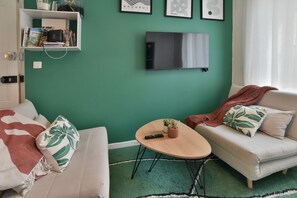 Ein Wohnzimmer mit grüner Wand, einem Flachbildfernseher, einem Sofa, einem Couchtisch und einem Bücherregal.