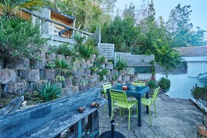 A patio with a table and chairs, surrounded by a stone wall with plants. - Flore - au cœur du bassin d'Arcachon (Arcachon)