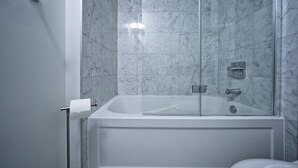 Un baño moderno con una bañera rodeada de vidrio, paredes de mármol y un dispensador de papel higiénico a la vista.