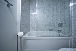 Ein modernes Badezimmer mit einer Glaskabine, Marmorwänden und einem sichtbaren Toilettenpapierhalter.