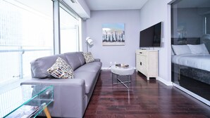 Una sala de estar moderna con un sofá gris, una mesa de centro de vidrio, un televisor y una cama con separador de vidrio.
