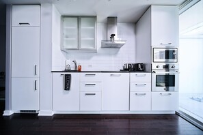 Eine moderne Küche mit weißen Schränken, einer Edelstahl-Dunstabzugshaube und integrierten Geräten, darunter eine Mikrowelle und ein Backofen.