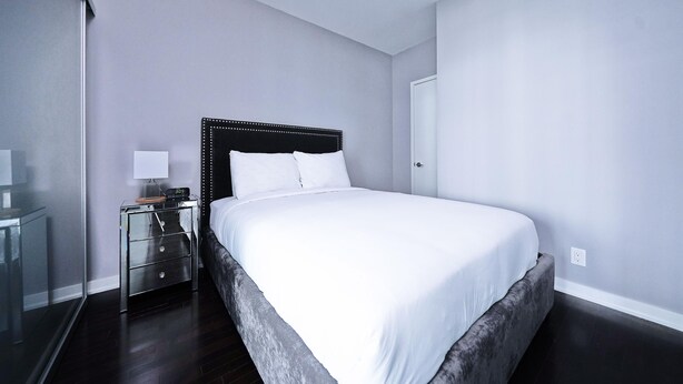 Un dormitorio moderno con una cama grande, una mesita de noche con una l ámpara y un espejo.