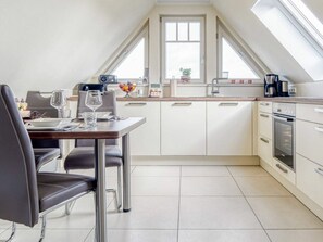 A modern kitchen with a dining area, featuring a dining table set for two, a built-in oven, and a large window providing natural light. - Kavelweg 9 Apt. 5 (Zingst)