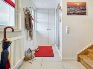 A hallway with a red carpet, a coat rack with hanging clothes, a wooden cane, a bag, and a pair of shoes. - Kavelweg 9 Apt. 5 (Zingst)