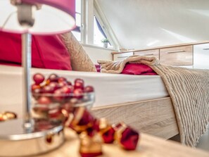 A bedroom with a bed, a bedside table with a lamp, and a window. - Kavelweg 9 Apt. 5 (Zingst)