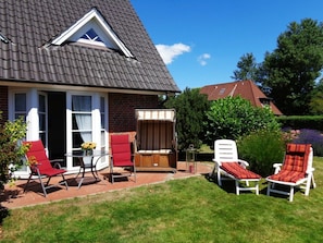 Ein Haus mit geneigtem Dach, einer Ziegel-Fassade und einer Terrasse mit Gartenmöbeln.