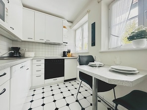 A compact kitchen with white cabinets, a black dishwasher, and a black chair. - Holiday Home With 1 Bedroom (St. Peter-Ording)