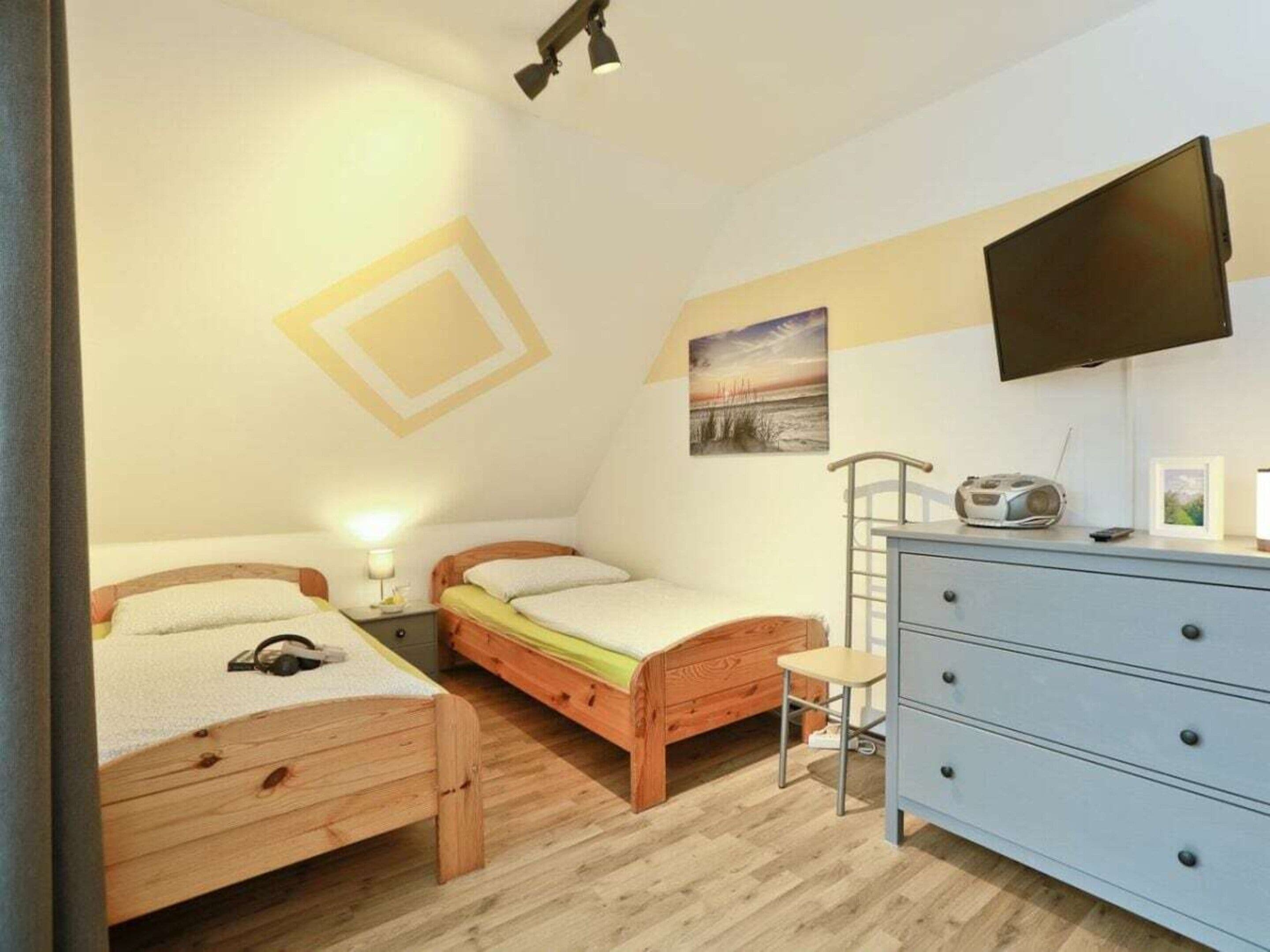 Une chambre à coucher avec deux lits en bois, une commode, une chaise, un téléviseur fixé au mur et un tableau représentant une plage.