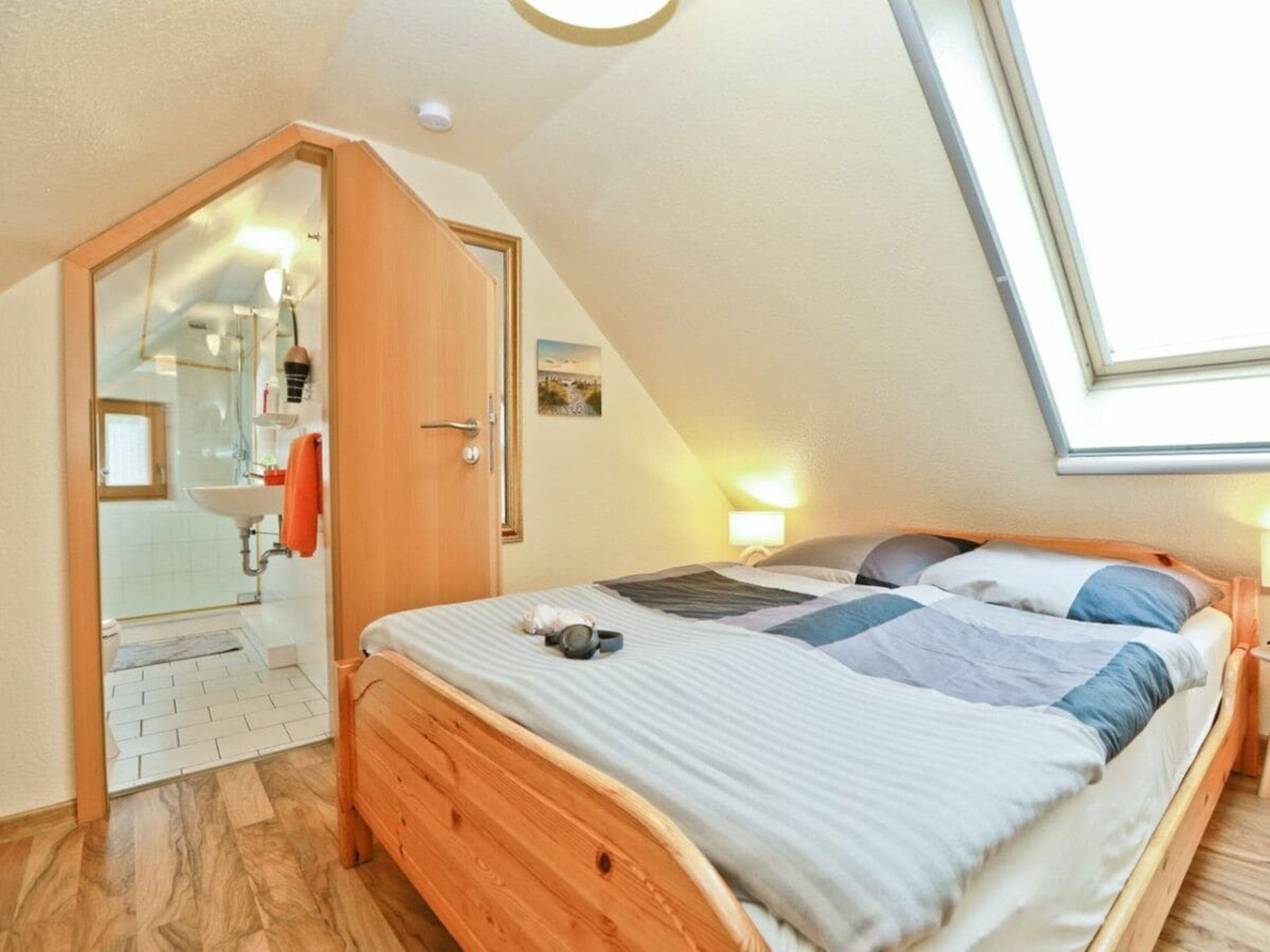 Une chambre avec un plafond en pente, un lit avec un cadre en bois, une table de chevet et une fenêtre laissant entrer la lumière naturelle.