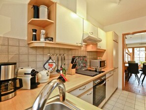 Eine moderne Küche mit Mikrowelle, Wasserkocher und Kaffeemaschine. Durch einen offenen Durchgang ist ein Essbereich zu sehen.