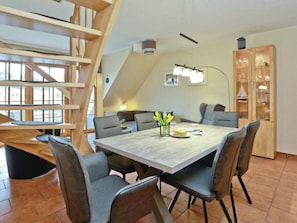 A dining area with a wooden table, grey chairs, and a staircase. - 1.4/t1 in the "freesenbruch" Holiday Park (Zingst)