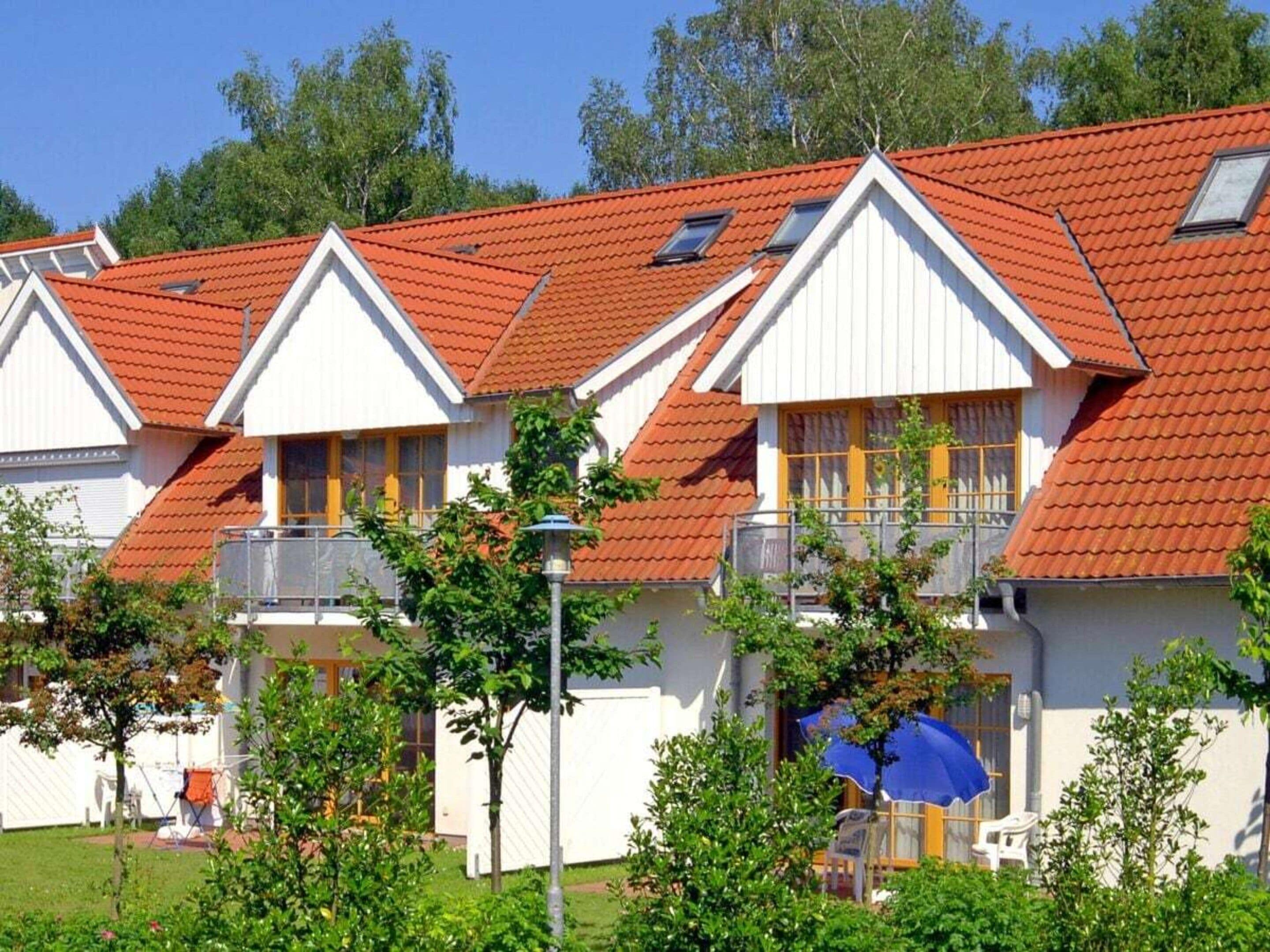 En rad vita byggnader med röda tak och balkonger, omgivna av grönska.