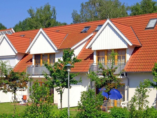 A row of white buildings with red roofs and balconies, surrounded by greenery. - 1.4/t1 in the "freesenbruch" Holiday Park (Zingst)