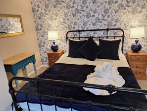 A bedroom with a metal bed frame, two bedside tables with lamps, a wooden nightstand, and a blue chair. - Fryers Cottage (Scarborough)