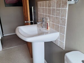 A bathroom with a white pedestal sink, a wooden door, and a tiled wall. - Fryers Cottage (Scarborough)