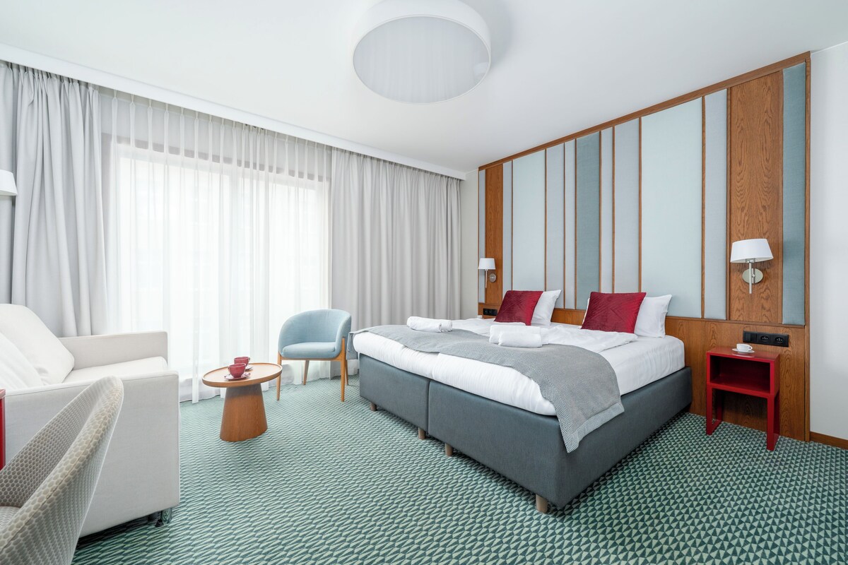 Een hotelkamer met een groot bed, een zithoek met een stoel en een tafel, en een wand van houten panelen.