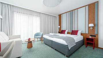 A hotel room with a large bed, a sitting area with a chair and table, and a wooden panel wall.