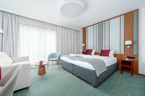 Een hotelkamer met een groot bed, een zithoek met een stoel en een tafel, en een wand van houten panelen.
