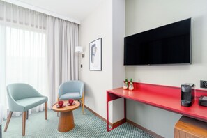 A hotel room with a TV, two chairs, a small table with drinks, and a red desk. - PERON 12 GWARNA (Wrocław)