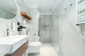 Een moderne badkamer met een douche met glazen wand, een wit toilet en een wastafelmeubel met een spiegel en wastafel.