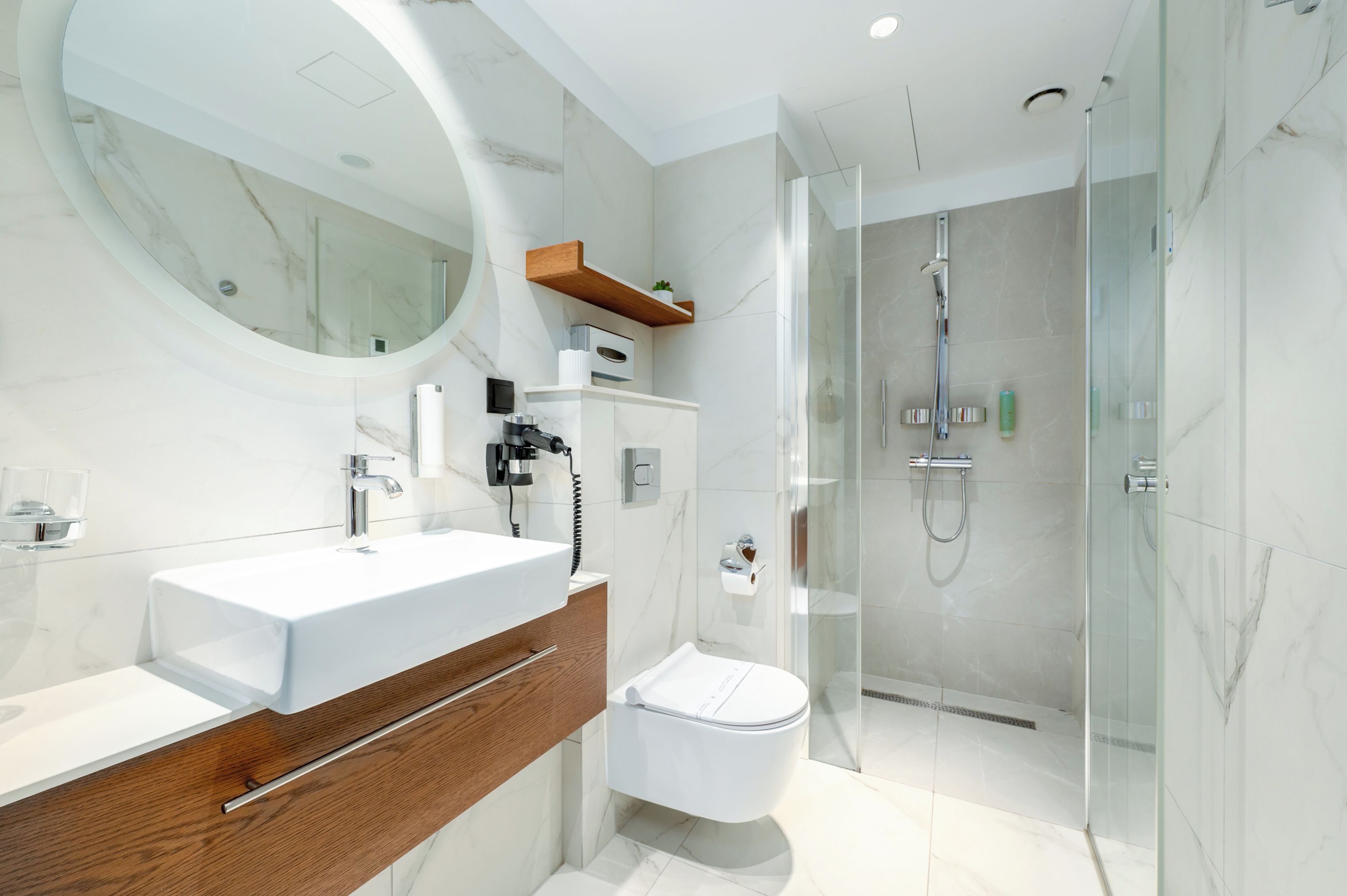 Un baño moderno con un espejo grande, dos lavamanos, un inodoro y zona de ducha con mampara de vidrio.