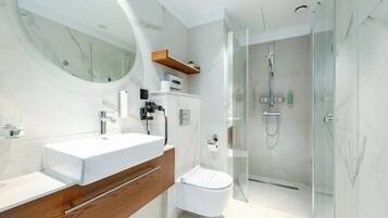 Et stilfuldt badeværelse med et stort spejl, to håndvaske, et toilet og en bruseniche med glasvægge.