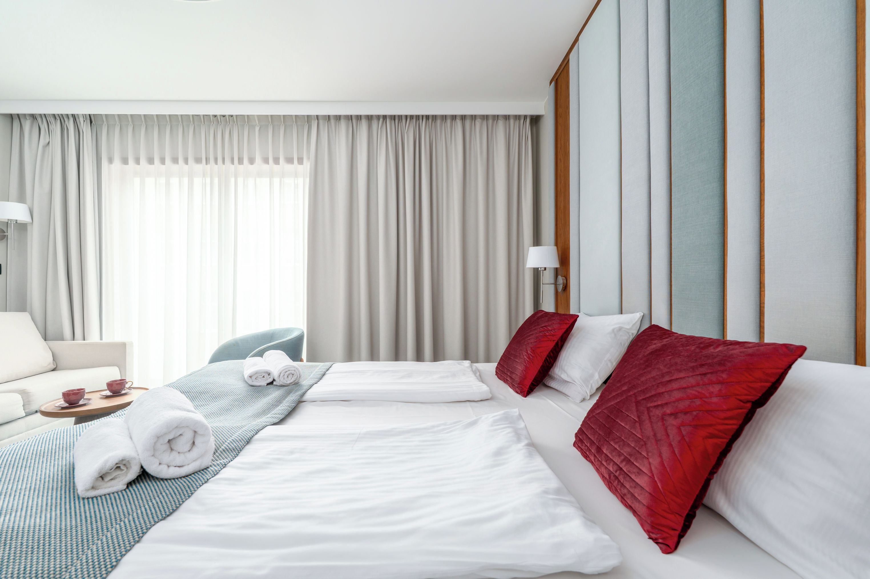 Habitación de hotel con dos camas, un sofá, una silla y un ventanal con cortinas.