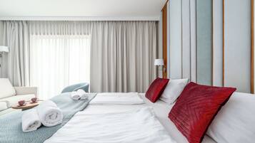 A hotel room with two beds, a sofa, a chair, and a window with curtains.