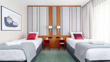 A hotel room with two beds, a wooden panel wall, a framed picture, two bedside lamps, and a view of the outdoors.