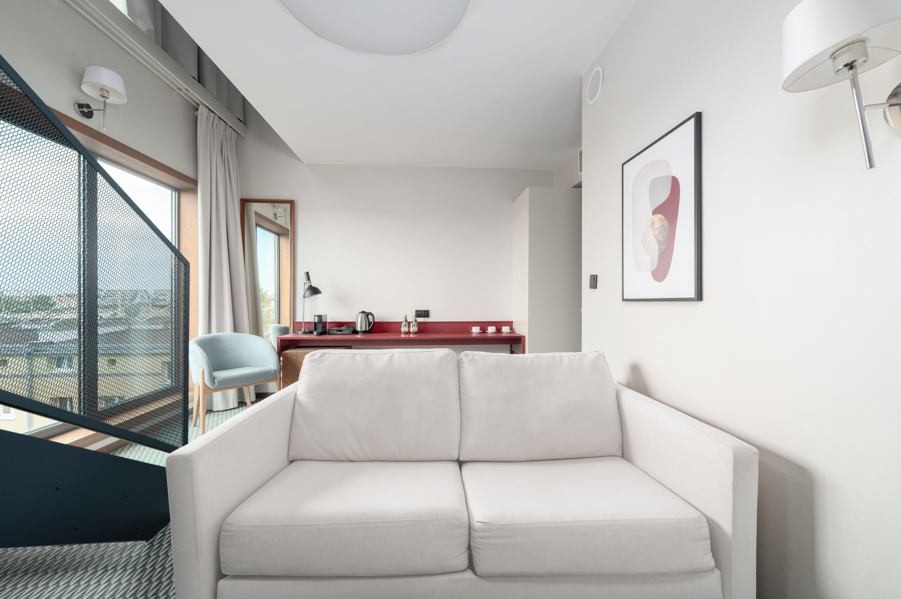Una sala de estar moderna con un sofá blanco, una consola roja con una cafetera y un ventanal con vistas.
