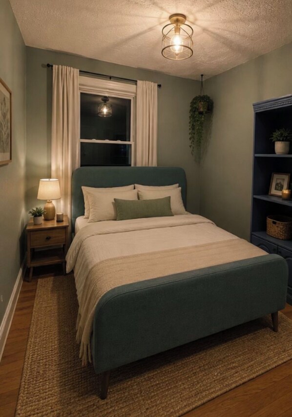 A bedroom with a bed, nightstand, lamp, window with curtains, and a hanging plant.